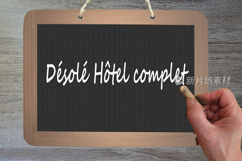 手握粉笔在满是石板的酒店写法语“Désolé Hôtel complete”